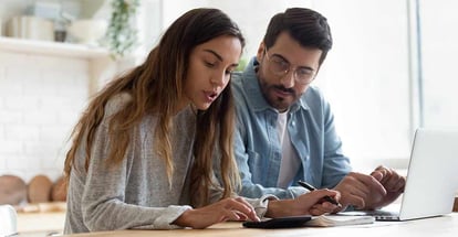 Wife and husband planning budget for mortgage payment using calculator sitting at table in kitchen